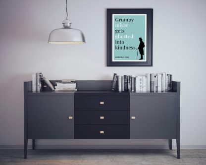 Humorous Christmas Carol print in black frame on wall, with black sideboard and books below. From Bookish Prints collection by StrangeBooks UK