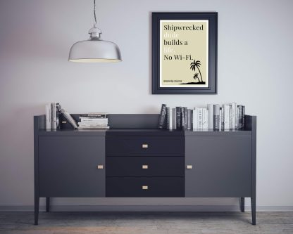 Humorous Robinson Crusoe print in black frame on wall, with black sideboard and books below. From Bookish Prints collection by StrangeBooks UK