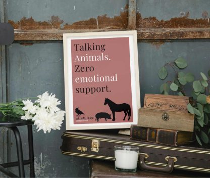 Humorous Animal Farm print in white wooden frame, perched on a violin case next to some books. From Bookish Prints collection by StrangeBooks UK