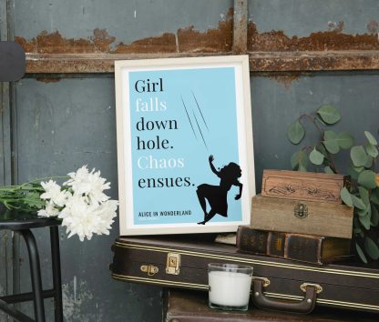 Humorous Alice in Wonderland print in white wooden frame, perched on a violin case next to some books. From Bookish Prints collection by StrangeBooks UK