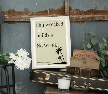 Humorous Robinson Crusoe print in white wooden frame, perched on a violin case next to some books. From Bookish Prints collection by StrangeBooks UK