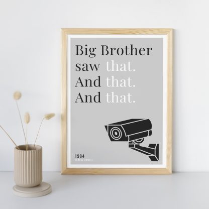 Humorous 1984 print in wooden frame, leaning against a plain wall. Small beige decoration nearby. From Bookish Prints collection by StrangeBooks UK