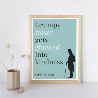 Humorous Christmas Carol print in wooden frame, leaning against a plain wall. Small beige decoration nearby. From Bookish Prints collection by StrangeBooks UK
