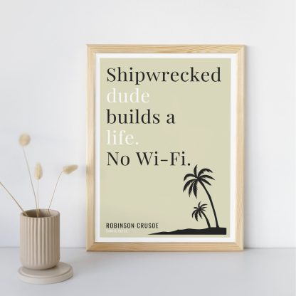 Humorous Robinson Crusoe print in wooden frame, leaning against a plain wall. Small beige decoration nearby. From Bookish Prints collection by StrangeBooks UK