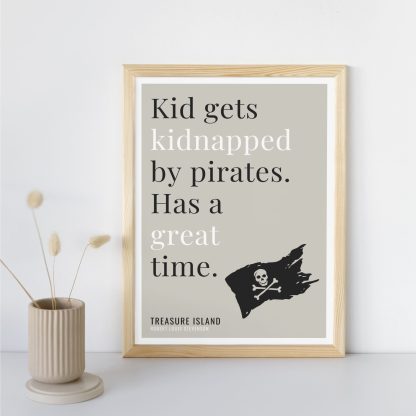 Humorous Treasure Island print in wooden frame, leaning against a plain wall. Small beige decoration nearby. From Bookish Prints collection by StrangeBooks UK