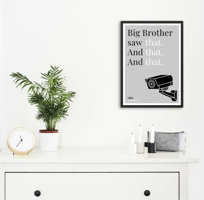 Humorous 1984 print in black frame on wall, with white chest of drawers and plants and candles below. From Bookish Prints collection by StrangeBooks UK