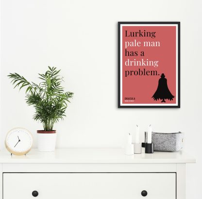 Humorous Dracula print in black frame on wall, with white chest of drawers and plants and candles below. From Bookish Prints collection by StrangeBooks UK