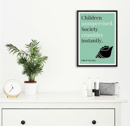 Humorous Lord of the Flies print in black frame on wall, with white chest of drawers and plants and candles below. From Bookish Prints collection by StrangeBooks UK