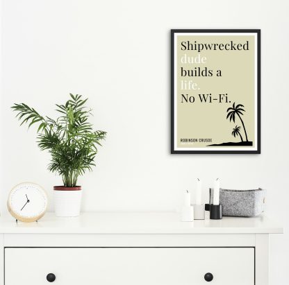 Humorous Robinson Crusoe print in black frame on wall, with white chest of drawers and plants and candles below. From Bookish Prints collection by StrangeBooks UK
