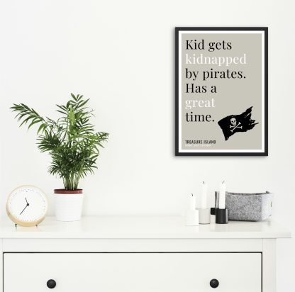 Humorous Treasure Island print in black frame on wall, with white chest of drawers and plants and candles below. From Bookish Prints collection by StrangeBooks UK