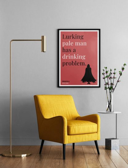 Humorous Dracula print in black frame on wall, with a yellow armchair in front next to a tall angular lamp and plant on a table. From Bookish Prints collection by StrangeBooks UK