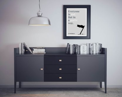 Humorous Les Misérables print in black frame on wall, with black sideboard and books below. From Bookish Prints collection by StrangeBooks UK
