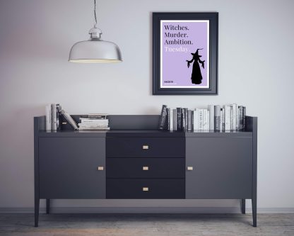 Humorous Macbeth print in black frame on wall, with black sideboard and books below. From Bookish Prints collection by StrangeBooks UK