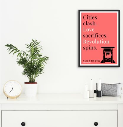 Humorous A Tale of Two Cities print in black frame on wall, with white chest of drawers and plants and candles below. From Bookish Prints collection by StrangeBooks UK